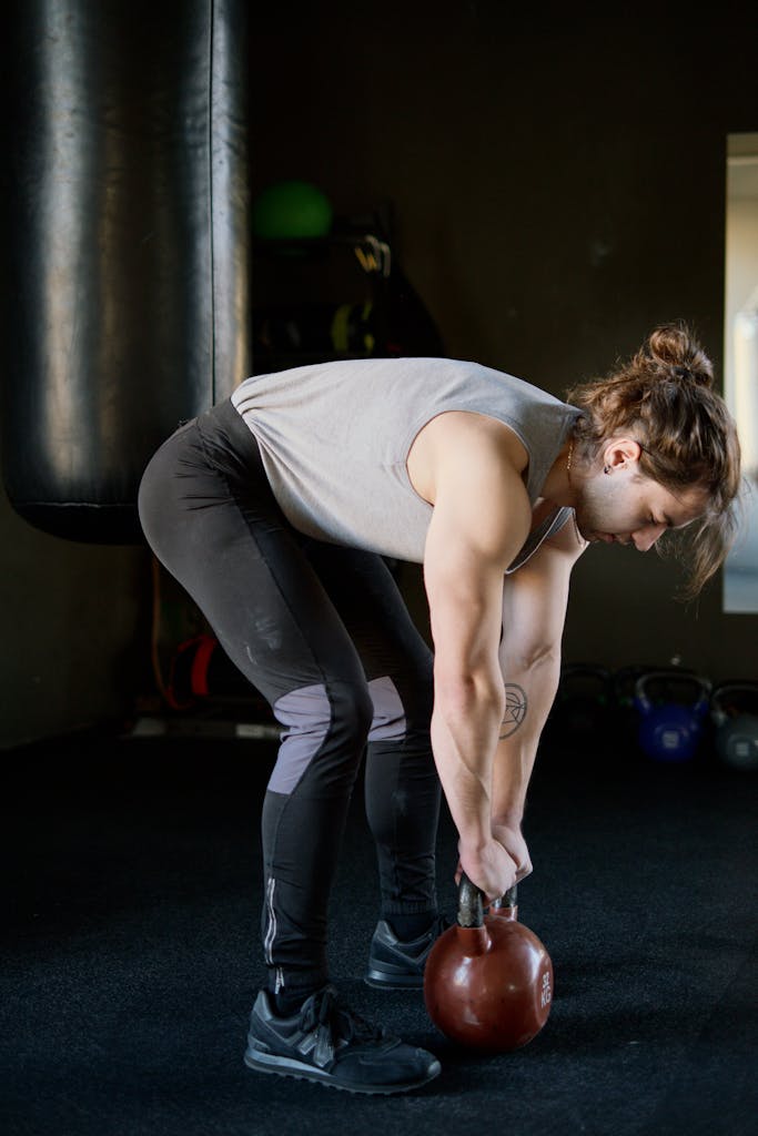 Athletic male engaged in a kettlebell deadlift for strength training indoors.